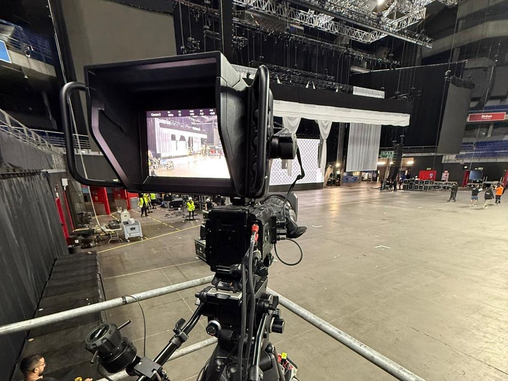Cámara broadcast con visor de estudio apuntando al escenario durante el montaje de un evento