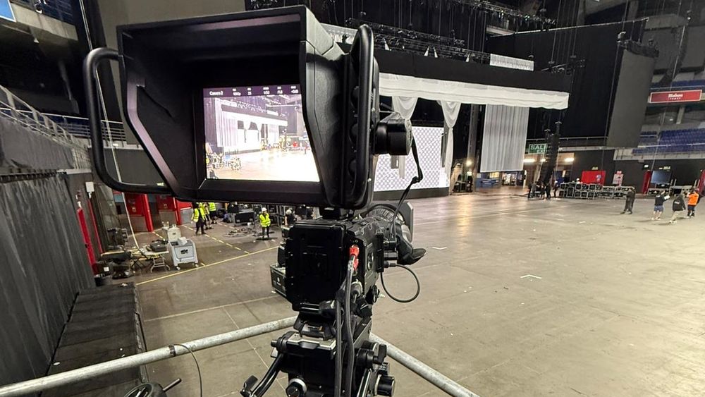 Cámara broadcast con visor de estudio apuntando al escenario durante el montaje de un evento