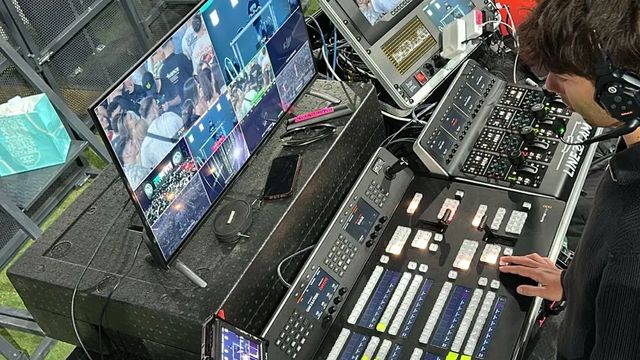 Realizador operando el panel de mezcla ATEM durante un festival, con el multiviewer y el público al fondo